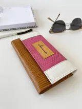 Billetera de cuero con estampado reptil en color marrón y fucsia con detalles en blanco. Tiene un sistema de cierre con broche y monedero externo.