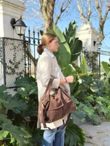 Bolso de cuero marrón con diseño tipo morral, cuenta con doble correa de hombro y correa larga ajustable, cierre superior y detalles de remaches metálicos.