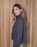 Camisa de manga larga con estampado de cuadros en tonos azules y rojizos. Presenta un cuello alto con volados y puños elásticos con detalle de volado en el extremo. Cierre frontal con botones ocultos.
