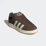 Championes Adidas Campus 00s de color marrón, confeccionados en cuero con las icónicas tres tiras dentadas en color blanco. Presentan una suela de caucho en tono crema y detalles en dorado, con un diseño inspirado en la cultura urbana y el skate de los años 2000.