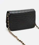 Bolso pequeño estructurado color negro, con textura capitoneada, asa de cadena y solapa frontal con botón a presión. Incluye divisor interno con cremallera.
