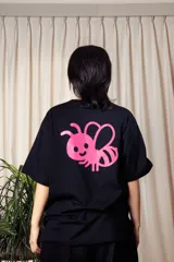 Remera negra de mangas cortas con estampa pequeña en el pecho de una abeja rosa con alas y la palabra "Tranca" en amarillo.