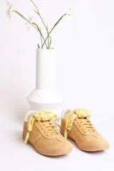 Zapatillas bajas color beige con detalles en marrón claro. Presentan cordones con pañuelos estampados en amarillo y blanco.