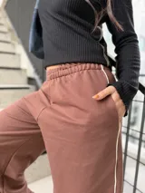 Pantalón deportivo estilo baggy de mujer, color chocolate, con cintura elástica y una línea lateral blanca.