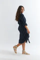 Vestido camisero midi de lino color azul marino con rayas verticales blancas, corte holgado, cuello camisero, mangas 3/4 con puños elásticos y lazo en la cintura.
