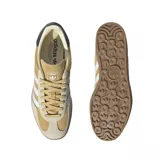 Championes adidas Gazelle Indoor, confeccionados en gamuza color tostado con las icónicas tres tiras laterales en blanco. Presentan suela de goma color marrón, detalle de talón en azul oscuro y el nombre del modelo en dorado.