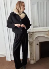 Chaqueta negra de corte corto y holgado, confeccionada con mezcla de lana. Cuenta con cuello ancho y solapa de piel sintética en tono beige claro, cierre frontal con botones oscuros y mangas largas amplias.