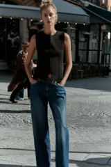 Top negro de punto, sin mangas, con cuello redondo. Presenta costuras marcadas en el frente y un bajo con abertura frontal que simula un peplum ajustado.