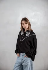 Camisa de color terracota con diseño de estilo western, presenta bordados blancos en la parte superior delantera y mangas largas abullonadas con puños ajustados. Cuenta con cierre frontal de botones y cuello camisero.