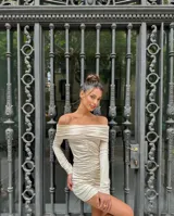 Vestido corto color chocolate con escote off-shoulder y mangas largas. Presenta frunces verticales en el frente.