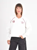 Buzo de cuello polo en color blanco, con mangas largas tipo raglán y detalles de costuras en color bordó. Presenta estampado frontal con el número 93 y un gráfico circular con texto.