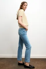 Jeans de mezclilla azul claro, tiro medio, corte recto y ligeramente acampanado en el bajo. Presenta cinco bolsillos y cierre frontal con cremallera y botón metálico.