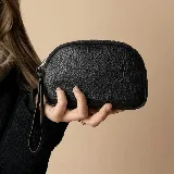 Mini sobre de mano con diseño semicircular, confeccionado en cuero texturizado negro. Cuenta con cierre superior y correa de muñeca integrada.