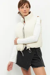 Chaleco puffer color beige, sin mangas, con cuello alto y cierre frontal con cremallera.