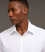 Camisa de manga corta con cuello inglés y cierre frontal abotonado, confeccionada en una mezcla de fibras de bambú, viscosa, poliéster y elastano. Presenta un diseño liso y entallado.