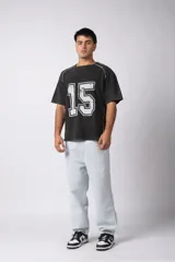 Remera de algodón con estilo deportivo, color verde oliva con efecto de lavado gastado. Presenta el número 15 estampado en blanco en el frente y detalles de costuras con vivos blancos en los hombros. Posee cuello redondo y corte holgado.