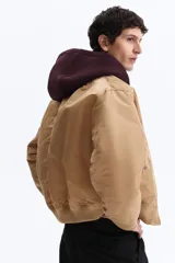 Campera bomber de nylon color tostado, con cuello, puños y bajo acanalados. Presenta cierre frontal, bolsillos laterales con botón a presión y un bolsillo con cierre en la manga.