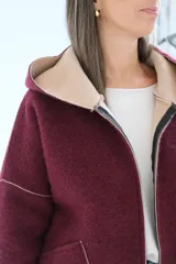 Tapado de paño bordó con interior en color beige, diseño con capucha, cierre frontal y bolsillos laterales. Presenta costuras visibles y puños vueltos que dejan ver el contraste de color.