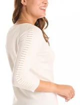 Buzo de tejido fino en color blanco, con cuello redondo y mangas tres cuartos tipo raglán. Presenta un detalle decorativo de tachas metálicas a lo largo de las mangas.