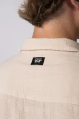 Camisa de hombre de manga corta color beige claro, confeccionada en lino. Tiene cuello clásico, cierre frontal con botones y corte recto.