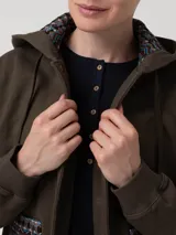 Buzo tipo campera de algodón orgánico color verde militar, con cierre frontal de botones a presión, capucha forrada con estampado étnico y bolsillos frontales con detalles de tejido aguayo multicolor.
