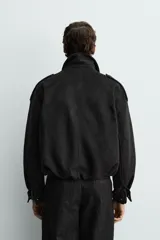 Cazadora cropped fit color verde militar, confeccionada en tejido efecto ante. Cuenta con cuello solapa, manga larga con puño abotonado, trabillas en los hombros, bolsillos laterales ocultos y un bolsillo interior. El bajo tiene elástico interior y el cierre frontal es con cremallera oculta por solapa con botones a presión.