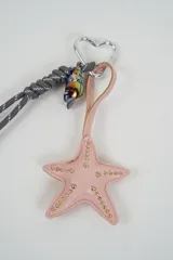 Llavero con mosquetón en forma de corazón, cordón negro trenzado, dije de caracol perlado y colgante de estrella blanca con tachas doradas.