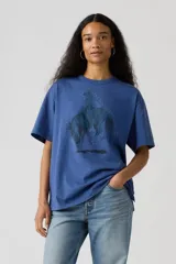 Remera de algodón color azul con estampa frontal de un cowboy montando un caballo, rodeado de pequeños puntos blancos. Presenta cuello redondo y mangas cortas con un corte holgado.