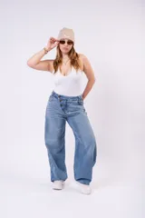 Pantalón de jean wide leg en lavado azul claro vintage, con corte amplio y fluido. Presenta un cierre asimétrico con botones expuestos en la parte delantera, talle alto y bolsillos funcionales.
