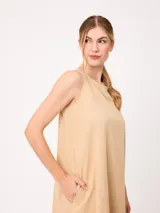 Vestido midi sin mangas de corte recto y holgado, color beige, con cuello redondo y bolsillos laterales.