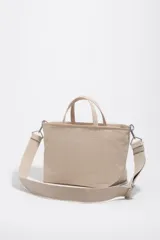 Bolso shopper mediano de mano Bimba y Lola color marrón, confeccionado en poliamida con detalles en cuero y herrajes metálicos dorados. Cuenta con doble asa de mano, correa de hombro ajustable de lona beige, cierre superior con cremallera y logo impreso en dorado al frente.