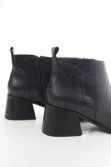Bota corta de cuero vacuno color marrón oscuro, con taco campana y detalle de textura símil cocodrilo en la parte trasera. Cuenta con cierre lateral y tirador en el talón.