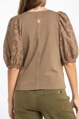 Remera de algodón color rosado con mangas cortas abullonadas de broderie con diseño floral calado. Presenta cuello redondo y costura vertical central en el frente.