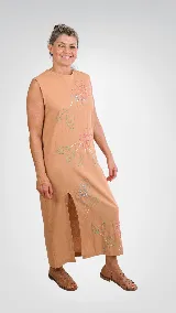 Vestido largo color tostado de corte recto y sin mangas, confeccionado en lino de algodón con bordados artesanales de flores en tonos rosados y hojas verdes, y un tajo frontal en la falda.