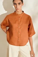 Camisa de lino color fucsia, con cuello mao, mangas cortas holgadas y cierre frontal con botones de madera. Cuenta con bolsillos frontales en el pecho.