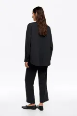 Camisa de corte oversize color negro, confeccionada en mezcla de algodón y lyocell con textura. Presenta cuello camisero, cierre frontal con botones, manga larga con puños abotonados y un bolsillo de plastrón en el pecho.