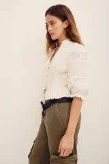 Camisa blanca de algodón con detalles de encaje broderie y transparencias, escote en V con cuello alto con volados, y mangas cortas abullonadas.
