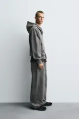 Sudadera con capucha y cierre de cremallera, de corte relajado (relaxed fit), confeccionada en algodón con interior afelpado. Presenta bolsillos frontales tipo canguro y acabados en rib. El tejido tiene un efecto lavado que le da un color negro desgastado.