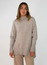 Sweater de punto color beige, de corte holgado y diseño oversize. Presenta cuello alto y puños con detalle de tejido trenzado, al igual que en el ruedo inferior.