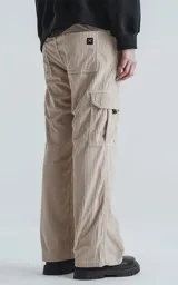 Pantalón cargo de corderoy color beige claro, de calce regular y pierna ancha, con múltiples bolsillos cargo laterales y etiqueta negra en uno de ellos.