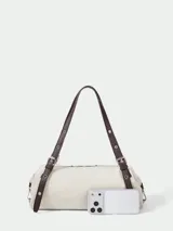 Cartera tipo shoulder bag de diseño cilíndrico, confeccionada en material sintético color crema con textura. Presenta correas largas ajustables en color marrón oscuro con detalles de hebillas y ojalillos metálicos.