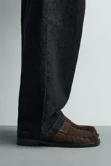 Mocasín de vestir para hombre, fabricado en piel con acabado serraje (gamuza) color marrón oscuro/café. Presenta un detalle de antifaz en el empeine con costuras visibles y horma cuadrada. La suela es negra y a contraste con un ligero tacón.