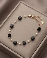 Pulsera de acero con baño de oro, adornada con cuentas cuadradas negras y pequeñas perlas blancas dispuestas alternadamente sobre una cadena eslabonada.