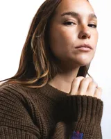 Buzo unisex de tejido de punto grueso en lana merino, color rojo, con cuello redondo y diseño de calce relajado. Presenta un detalle bordado a mano en contraste en la manga.