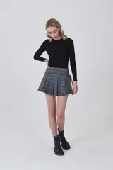 Falda corta plisada de poliéster con estampado tartán en tonos grises, azules y beige. Presenta un detalle de lazo o fajín anudado en la cintura.