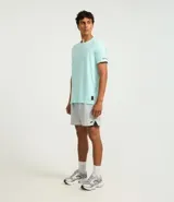 Remera deportiva de hombre con tecnología dry fit, cuello redondo y manga corta. Presenta un diseño liso en color beige con una pequeña etiqueta decorativa en el dobladillo.