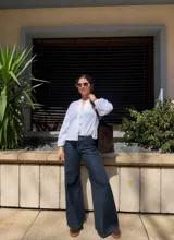 Camisa blanca de broderie con cuello redondo, cierre frontal con botones de madera y mangas largas abullonadas con puños elásticos.
