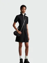 Vestido corto negro de algodón con cuello alto, cierre frontal con cremallera, mangas cortas, dos bolsillos con solapa en la falda y falda acampanada.