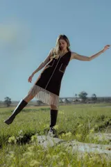 Vestido corto negro sin mangas, con escote en V y detalle de flecos en el ruedo. Presenta bordados en color blanco en el escote, los bolsillos y el centro del vestido.