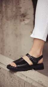 Sandalia de cuero color negro con combinación de texturas, base de goma liviana, diseño chunky, tiras anchas en el empeine y tira con hebilla ajustable en el tobillo.